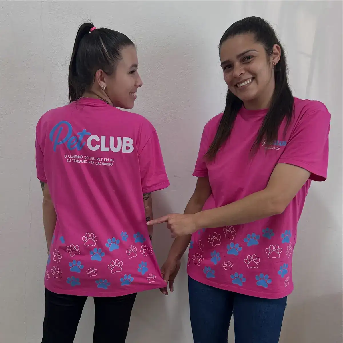 Duas pessoas da equipe mostrando o uniforme novo rosa com o logo do Pet Club e patinhas azuis